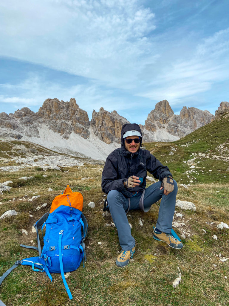 Marcin siedzi na trawie i pije herbatę z termosu, a obok niego leży plecak. Jest to koniec ferraty degli alpini.