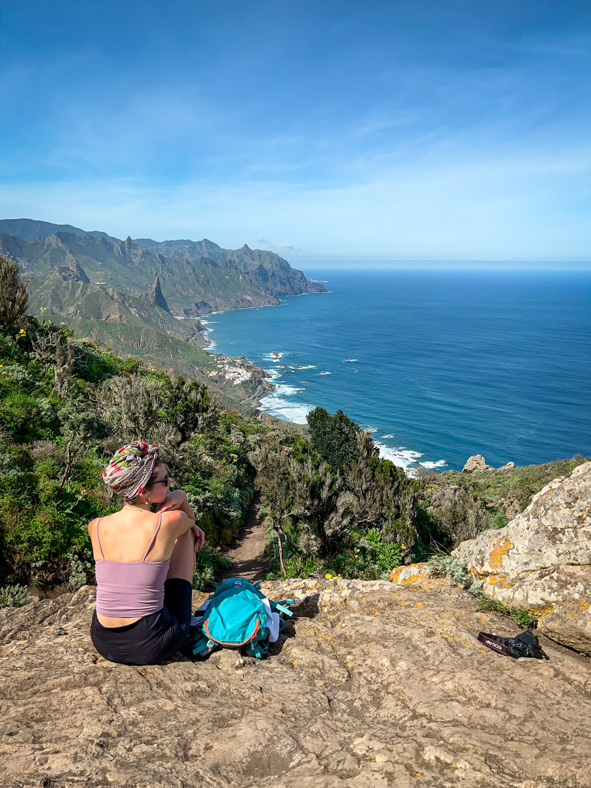 Ewa siedzi na punkcie widokowym na szlaku Benijo-El Draguillo, a przed nią widok na wybrzeże oceanu oraz miasteczko Taganana