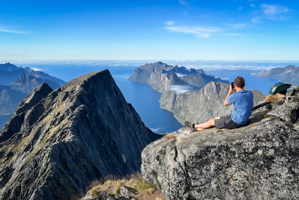 Marcin siedzi na płaskim kamieniu na szczycie Breitind. Wokół niesamowita panorama fiordów i szczytów gór. 